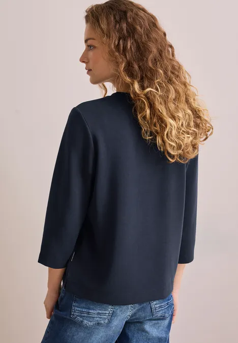 Frau mit lockigem Haar von hinten, trägt dunkelblauen Pullover und Jeans.